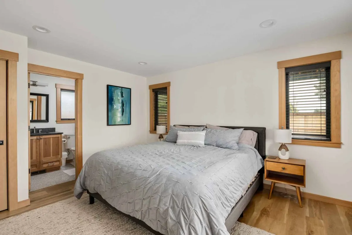A cozy king-sized bedroom with elegant artwork on the wall, a nightstand with a soft-glow lamp, and sunlight streaming in through the windows. The serene ambiance is ideal for relaxation and rejuvenation.