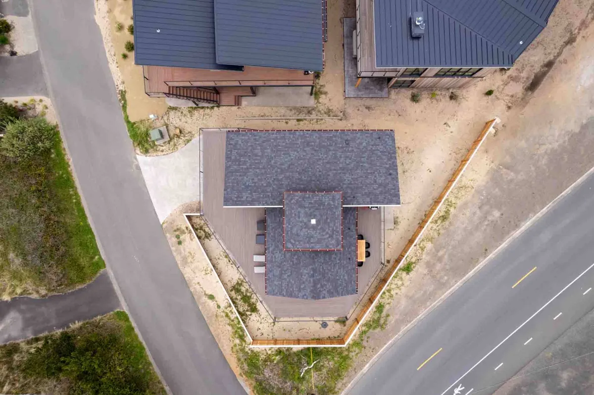 A modern exterior shot featuring a unique roof structure and surrounding landscaping, with a nearby road hinting at easy access to local attractions. The tranquil, contemporary mood suggests a stylish yet serene environment for guests seeking relaxation close to the heart of Manzanita.