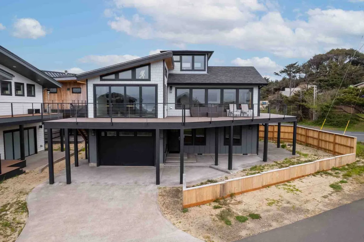 The modern home’s deck area, complete with large windows and sleek architectural lines, opens out to an inviting outdoor space. The view suggests a seamless transition from interior comfort to outdoor relaxation, ideal for gatherings, al fresco dining, or unwinding after a day at the shore.