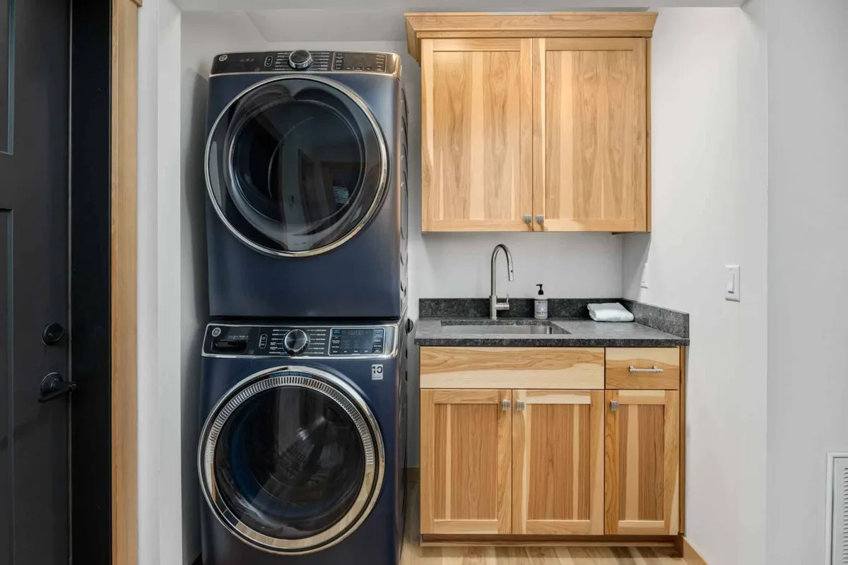 This image shows a laundry area featuring a modern washer and dryer, wood cabinetry, and a granite countertop. The space appears tidy and efficient, reflecting a focus on practical conveniences for guests.