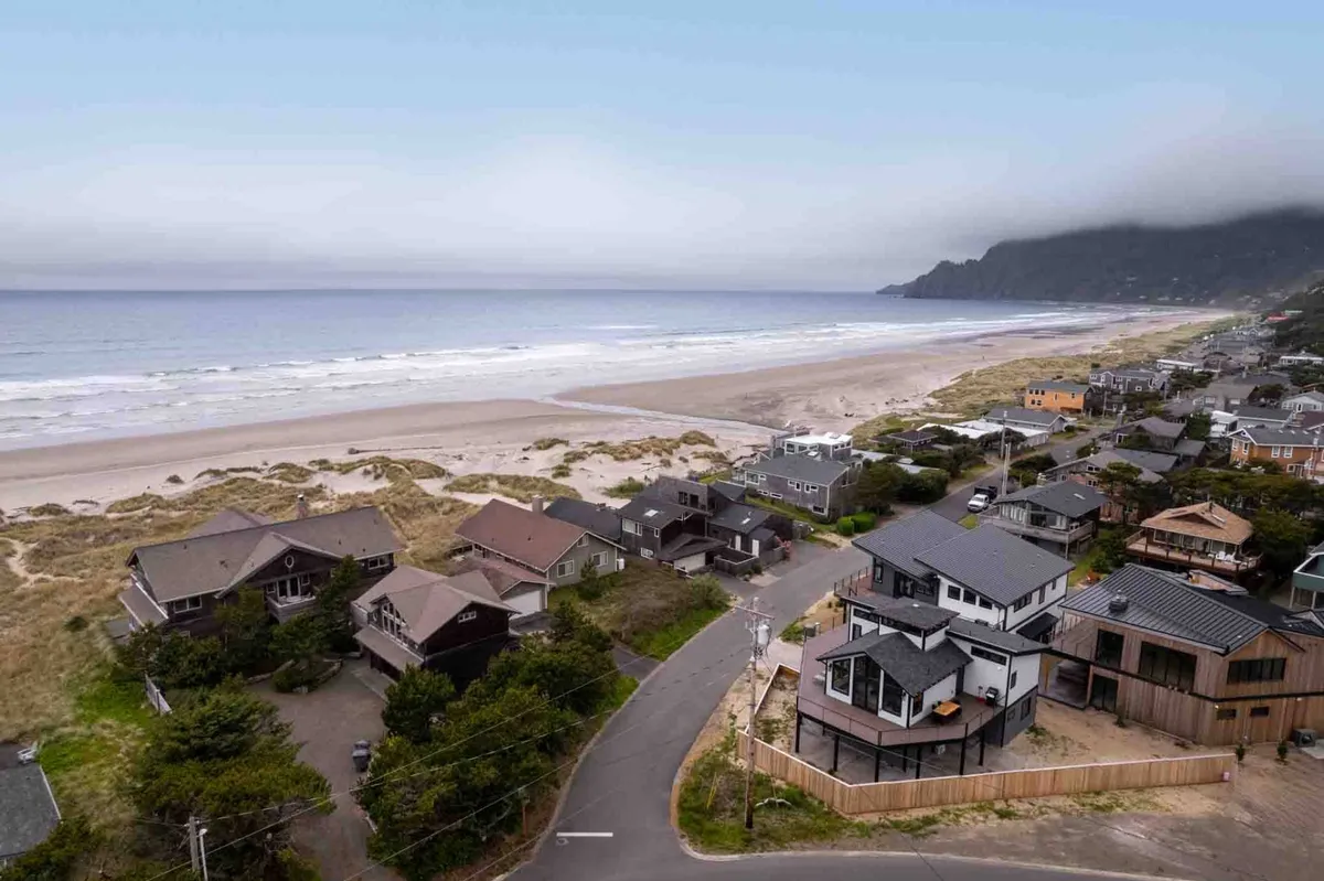 A breathtaking oceanfront scene featuring a wide sandy beach, gentle waves, and rolling dunes with residential homes nestled alongside coastal cliffs. The expansive view highlights the inviting shoreline and the easy beach access, echoing the sense of adventure and relaxation described in the section.
