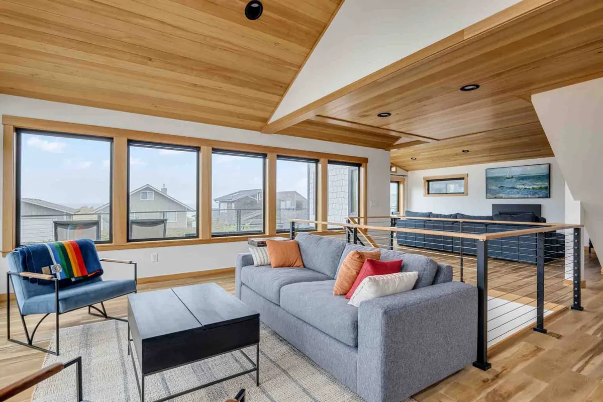 A cozy living space with a comfortable sofa, colorful throw blanket, and large windows showcasing beautiful views of the outdoors. The warm, inviting scene is ideal for relaxing, connecting with friends, or simply gazing at the landscape as evening falls.