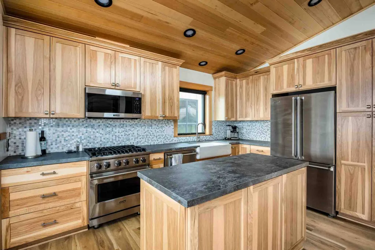 A contemporary kitchen centered around a large island, with sleek stainless steel appliances and a colorful mosaic backsplash adding warmth and visual interest. The open design encourages interaction, ideal for social meals and culinary activities.
