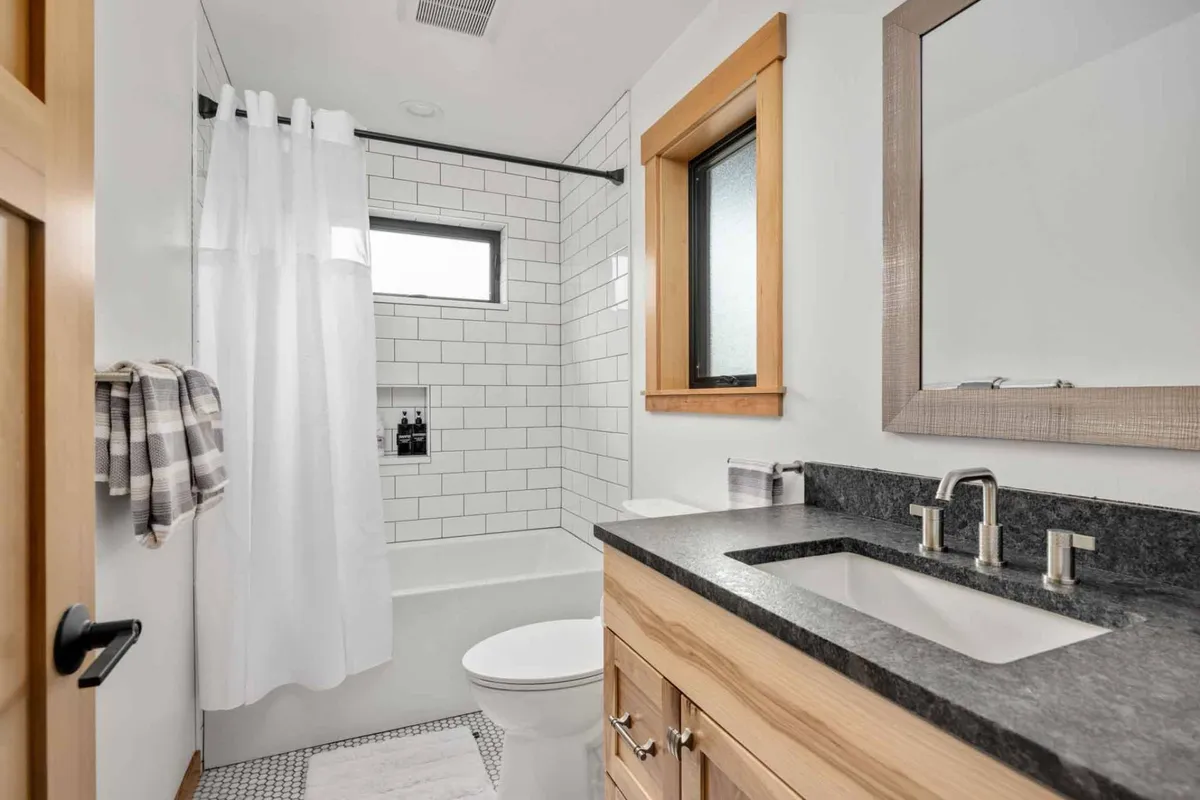 A modern en-suite bathroom with a spacious shower area, a sleek vanity with a sink and mirror, and a window bringing in gentle daylight. The room suggests a spa-like experience, perfect for unwinding after a busy day.